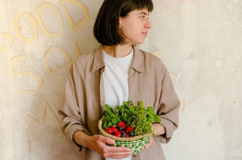 Woman standing with a basket of fresh greens and berries against a rustic wall background.