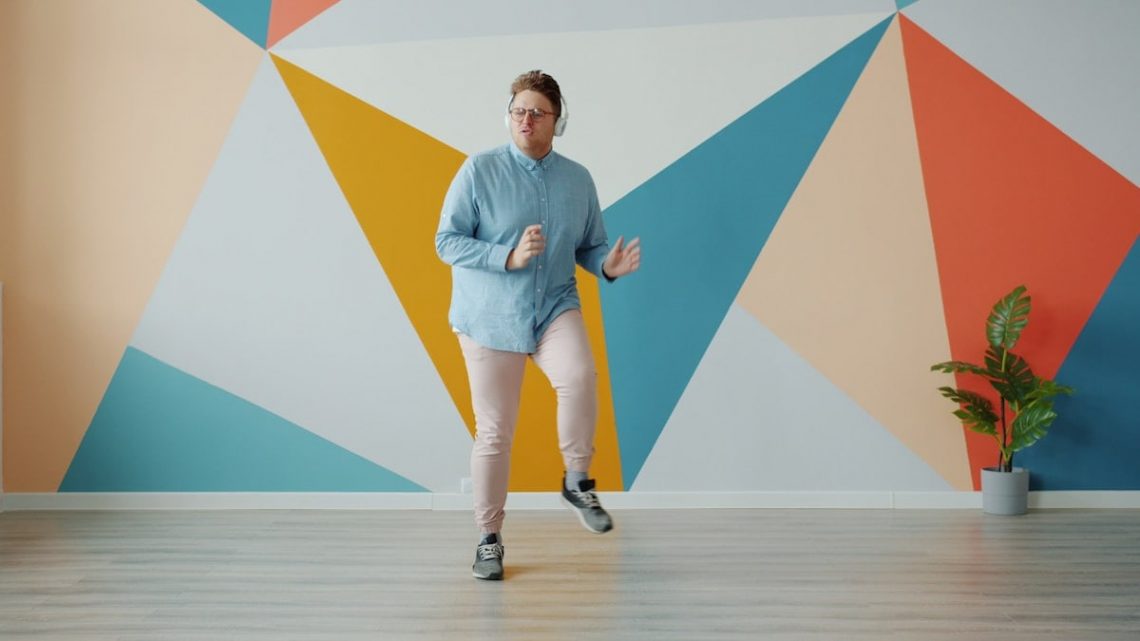 Modern guy is listening to radio through headphones dancing on colorful background alone enjoying music at home. Technology and lifestyle concept.