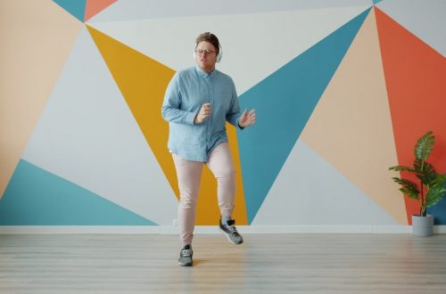 Modern guy is listening to radio through headphones dancing on colorful background alone enjoying music at home. Technology and lifestyle concept.